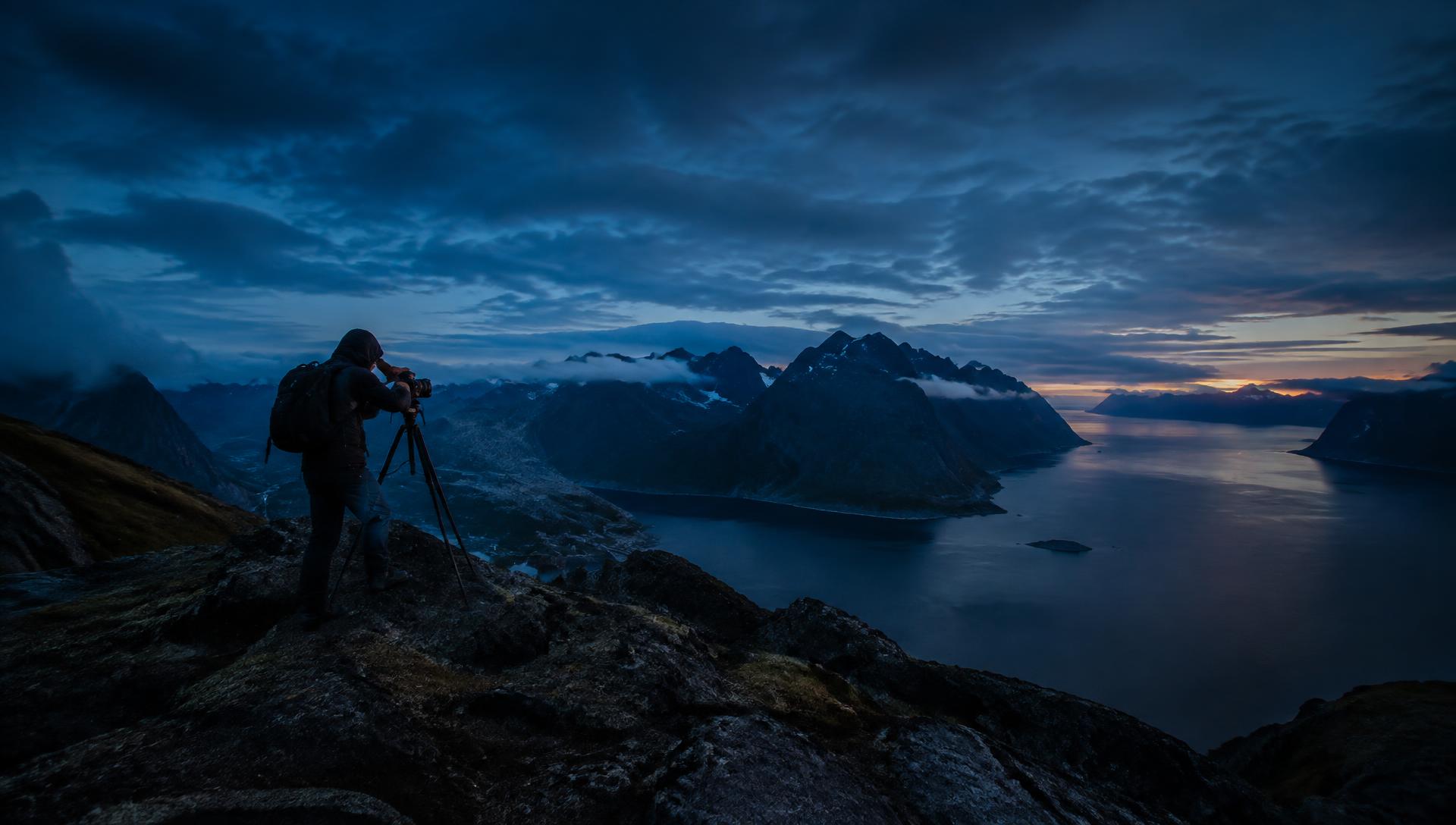 Landskapsfotograf med stativ på en fjälltopp vid blå timmen