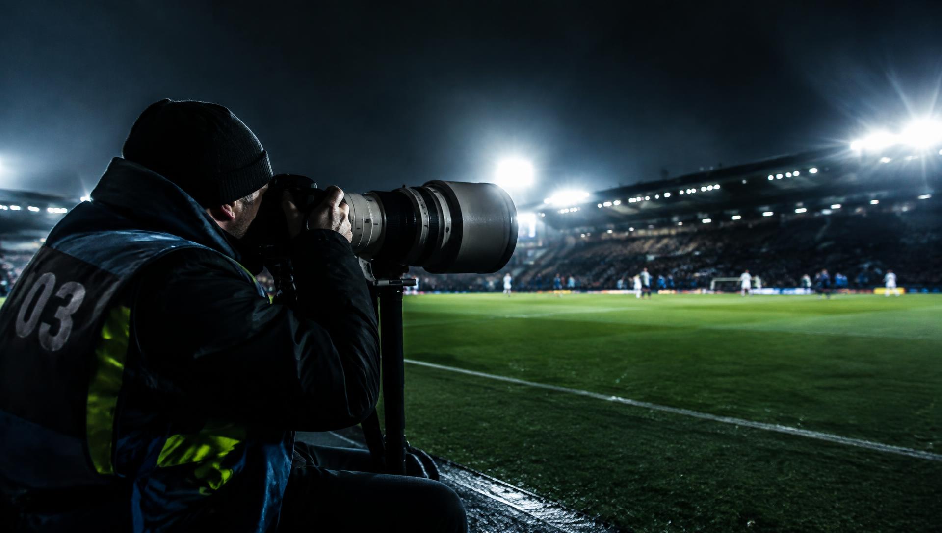 Sportfotograf med teleobjektiv vid en fotbollsplan i strålkastarljus